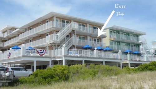 A beachfront hotel with two buildings, featuring balconies and blue umbrellas, labeled "Unit 32-4."