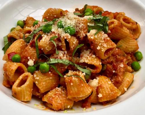 A bowl of pasta with a rich tomato sauce, green peas, and fresh basil, topped with grated cheese.