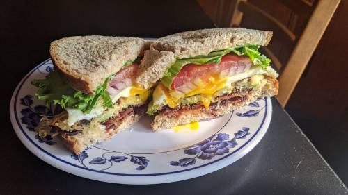 A hearty sandwich with layers of lettuce, tomato, egg, and bacon, served on whole grain bread, cut in half.