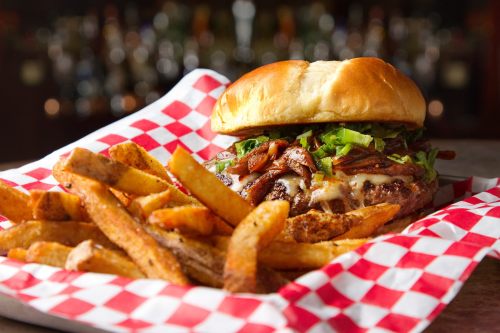 A juicy burger topped with bacon and lettuce, served with crispy fries in a red and white checkered basket.