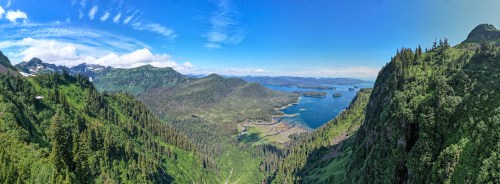 A panoramic view of lush green mountains and a serene blue bay under a clear sky.