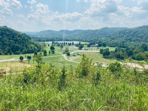 A scenic view of rolling green hills and a valley with trees and a small lake under a bright blue sky.