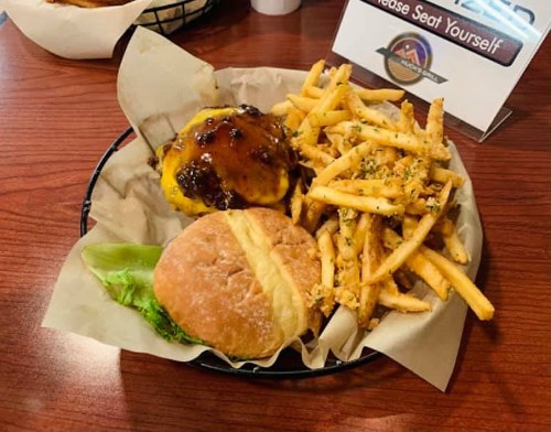 A plate with a cheeseburger topped with sauce, lettuce, and a side of golden fries on a wooden table.