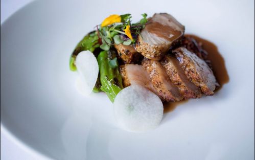 A beautifully plated dish featuring sliced meat, green vegetables, and garnishes on a white plate.