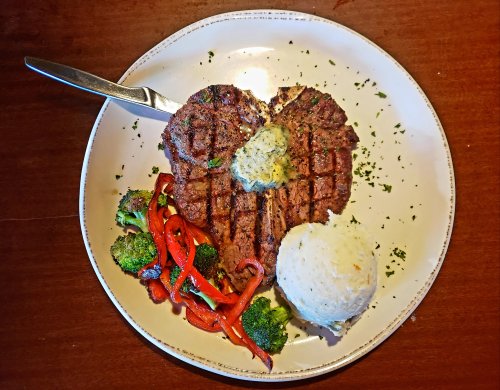 A grilled steak with herb butter, served with rice and sautéed broccoli and red peppers on a white plate.