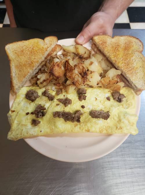 A plate with a fluffy omelet topped with ground meat, served with crispy potatoes and two slices of toasted bread.