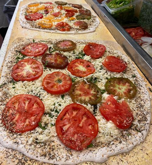 A freshly prepared pizza topped with sliced tomatoes and cheese on a wooden surface.
