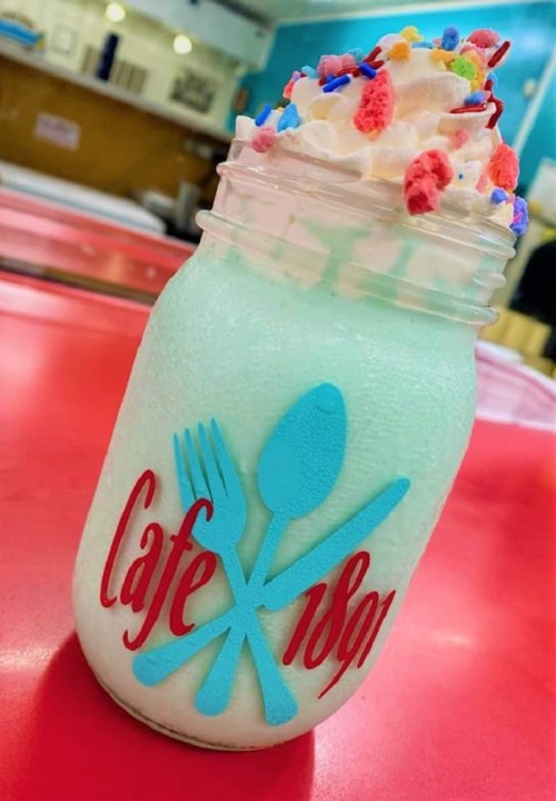 A colorful milkshake in a jar topped with whipped cream and sprinkles, featuring a "Cafe 1891" logo.