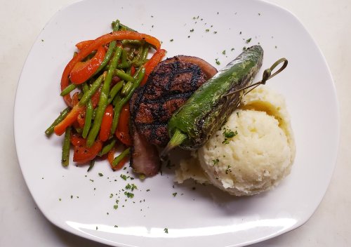 Grilled steak with mashed potatoes, grilled jalapeño, and sautéed green and red bell peppers on a white plate.