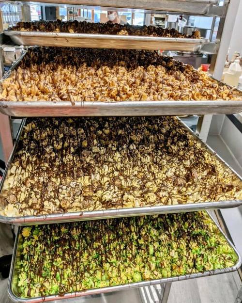 A stack of trays filled with colorful popcorn drizzled with chocolate and caramel, showcasing various flavors.