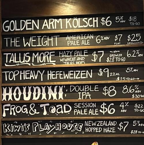 Menu board featuring various craft beers with prices and ABV percentages, including Kölsch, IPA, and pale ales.