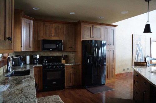 A modern kitchen featuring wooden cabinets, granite countertops, a black refrigerator, and stainless steel appliances.