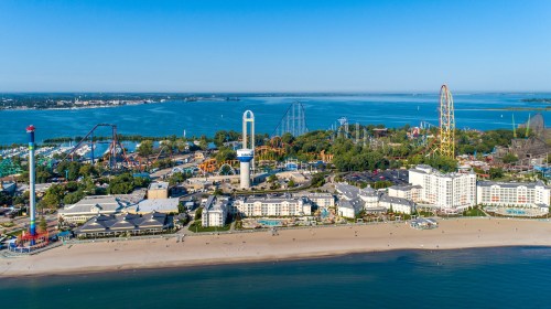 Aerial view of a beachside amusement park with rides, hotels, and a clear blue sky over a calm lake.