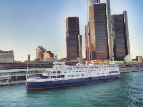 A large boat docked in a river with modern skyscrapers in the background during sunset.