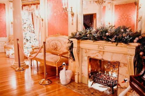 Elegant room with a marble fireplace, decorated for the holidays, featuring a Christmas tree and swan accents.