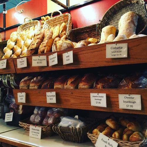 A display of various breads on wooden shelves, with price tags for each type, including ciabatta and sourdough.