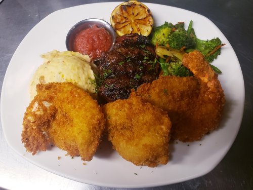 A plate featuring fried shrimp, grilled steak, mashed potatoes, sautéed vegetables, and a lemon wedge with sauce.
