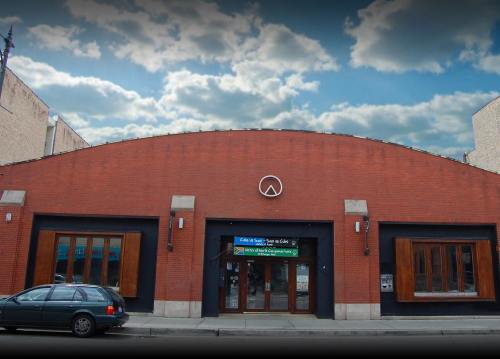 A brick building with large windows and a curved roof, under a cloudy sky. A car is parked in front.