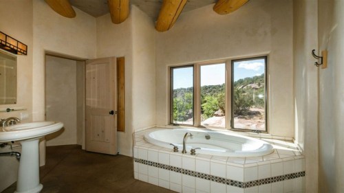 Bright bathroom featuring a large tub, window with scenic views, and rustic wooden beams.