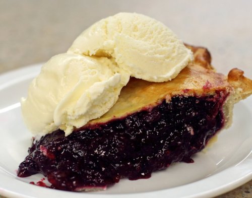 A slice of berry pie topped with a scoop of vanilla ice cream on a white plate.