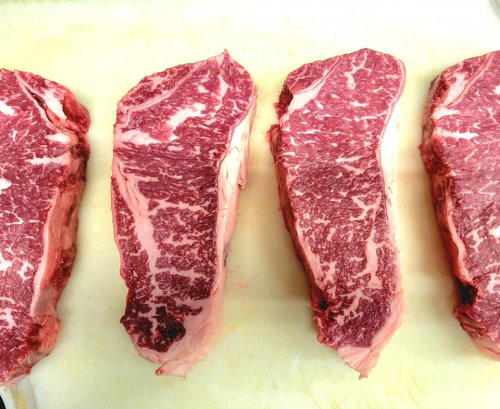 Four marbled cuts of beef steak arranged on a cutting board, showcasing rich red and white fat patterns.