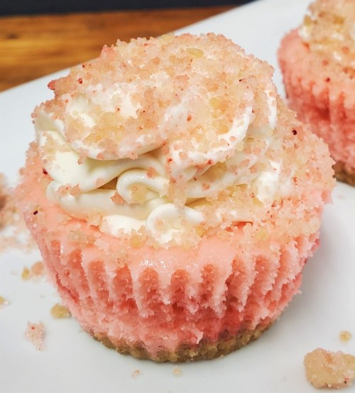 Close-up of a pink cupcake topped with white frosting and sprinkled with sugar crystals on a white plate.