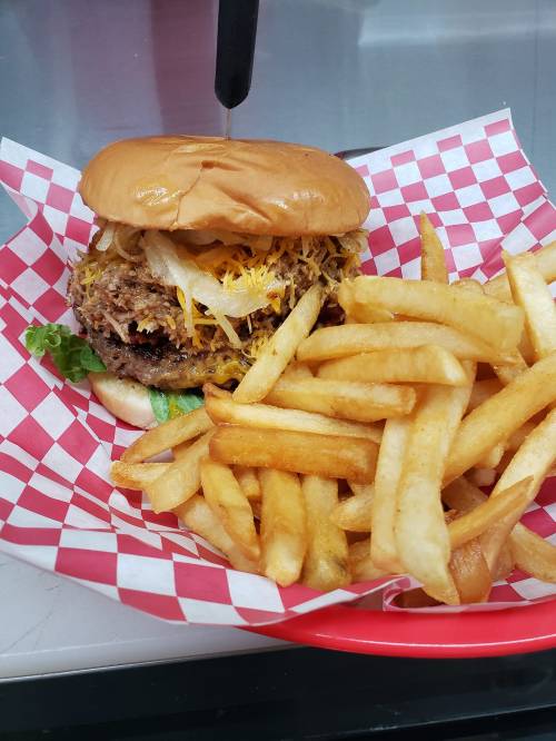A juicy burger topped with cheese, onions, and lettuce, served with a side of golden French fries in a red checkered basket.