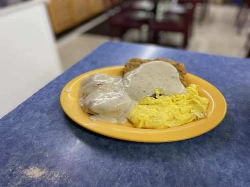 A plate of food featuring scrambled eggs, gravy, and a piece of fried chicken on a yellow plate.