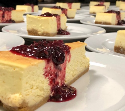 Slices of cheesecake topped with berry sauce, arranged on white plates.