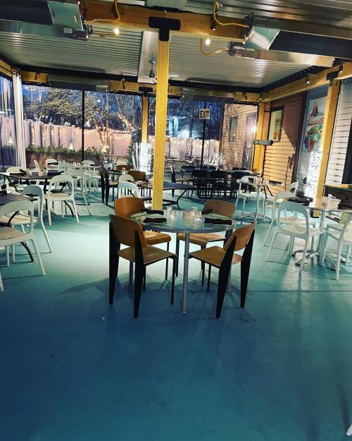 Empty restaurant patio with tables and chairs, featuring a turquoise floor and warm lighting.