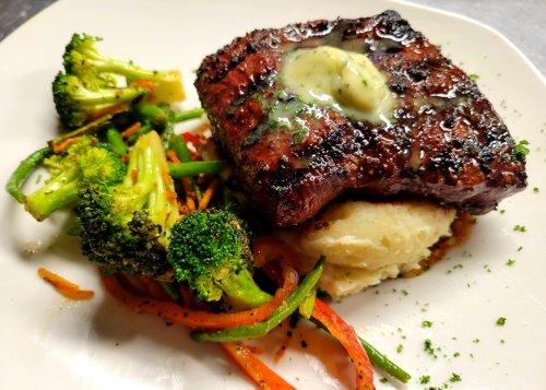 Grilled steak topped with herb butter, served with mashed potatoes and sautéed broccoli and mixed vegetables.