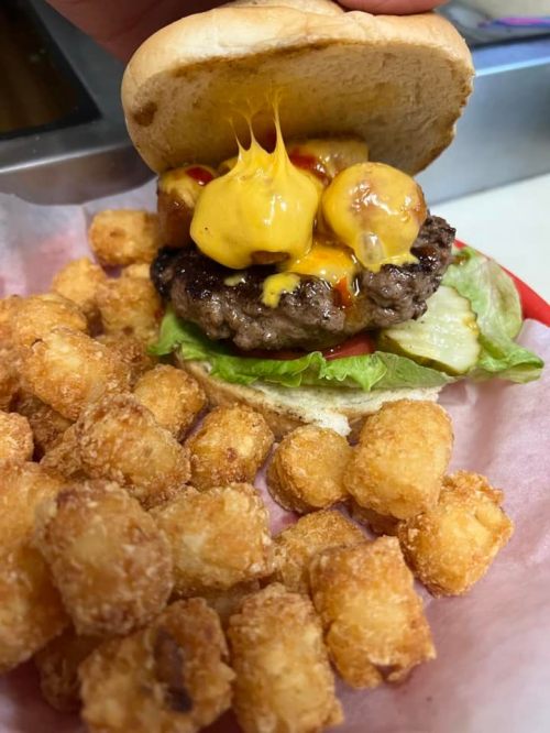 A juicy cheeseburger with melted cheese, lettuce, and tomato, served with a side of crispy tater tots.