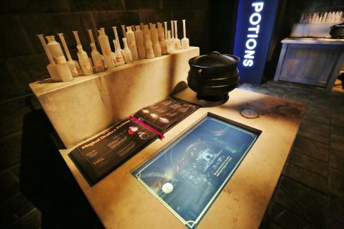 A potions display featuring glass bottles, a cauldron, and an interactive book on a stone table in a dimly lit room.