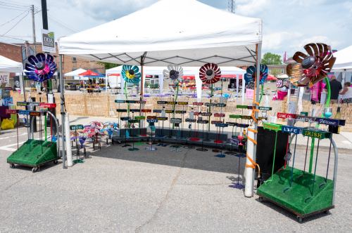 A colorful market stall with decorative signs and wind spinners, set up outdoors under a white tent.