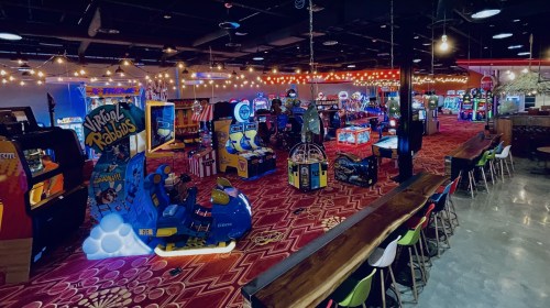 A vibrant arcade filled with colorful games and bright lights, featuring various arcade machines and a cozy seating area.