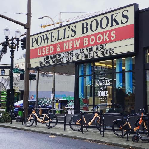 Sign for Powell's Books with a cafe, featuring bicycles parked outside and a city street view.