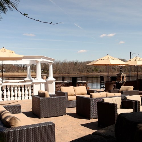 Outdoor seating area with wicker furniture and umbrellas, overlooking a calm water view under a clear blue sky.