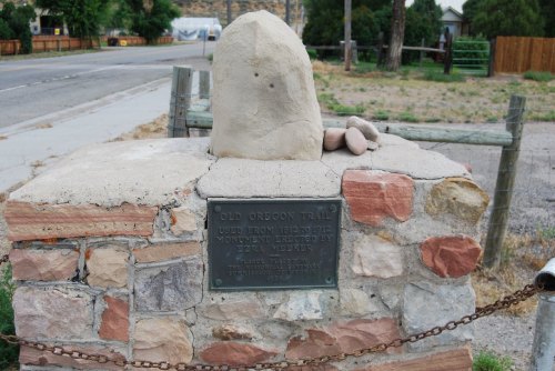 A stone monument with a plaque, marking the Old Oregon Trail, set near a road and surrounded by greenery.