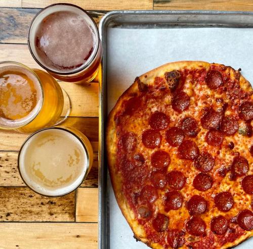 A pepperoni pizza on a tray next to four glasses of beer on a wooden table.