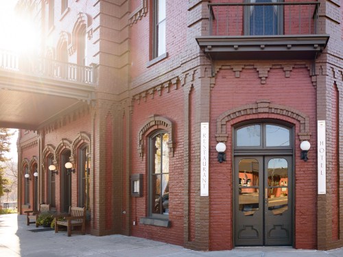 Historic red brick building featuring a restaurant and hotel entrance, with sunlight illuminating the facade.