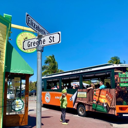 A street sign at the corner of Elizabeth and Greene St, with a trolley and people in Key West, Florida.