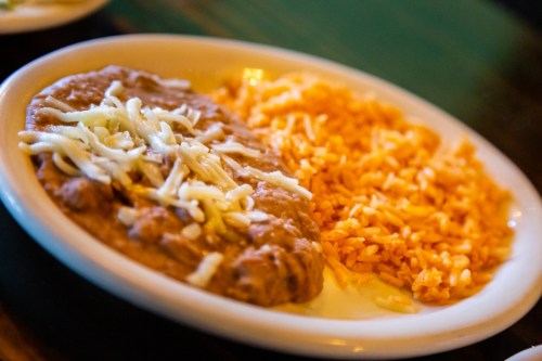 A plate of refried beans topped with cheese, served alongside orange rice.