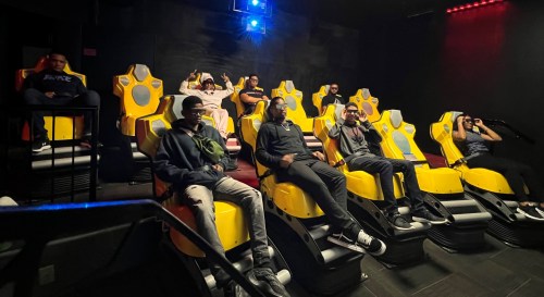 A group of people sitting in yellow motion seats in a dark room, preparing for an immersive experience.