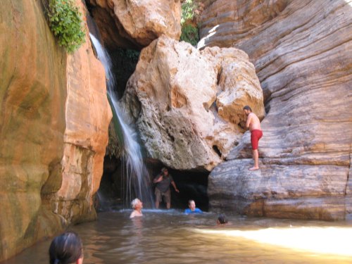 A group of people swimming in a natural pool surrounded by rocky cliffs and a small waterfall.