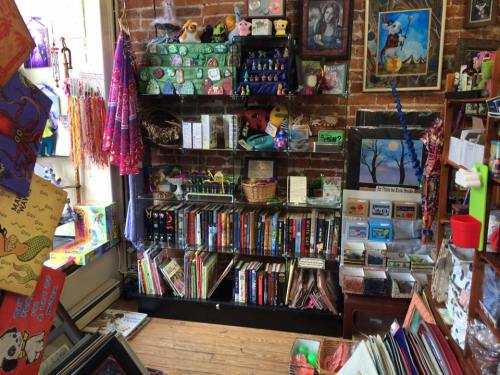 A cozy bookstore with colorful shelves, books, toys, and decorative items against a brick wall.