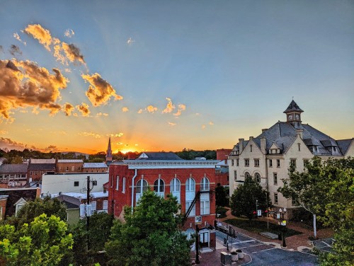 Sunset over a small town, featuring historic buildings, trees, and colorful clouds in the sky.