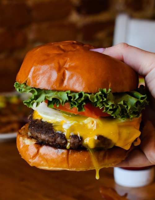 A hand holding a juicy cheeseburger with lettuce, tomato, and melted cheese on a toasted bun.