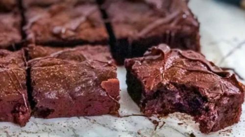 A close-up of rich chocolate brownies, with one piece partially eaten, on a parchment-lined surface.