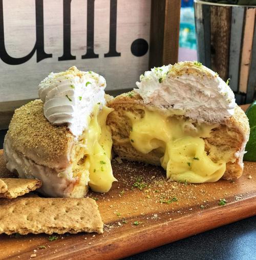 A close-up of a dessert with creamy filling, topped with whipped cream and graham cracker crumbs, on a wooden board.