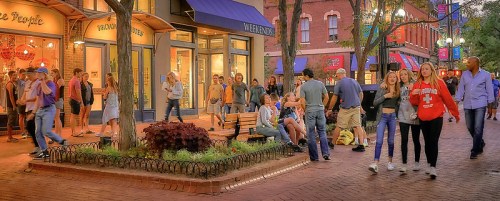 A lively street scene with people walking, sitting on benches, and enjoying the atmosphere in a vibrant urban area.